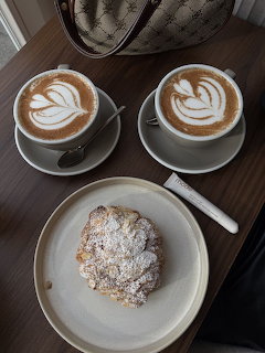 Two lattes with decorative foam art alongside a sugar-dusted croissant on white plates