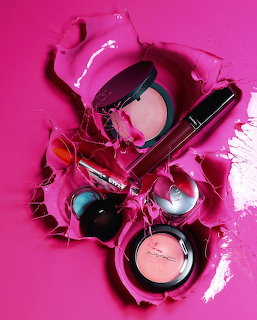 Various makeup products like compacts and lipstick arranged on a bright pink background with smeared cosmetics