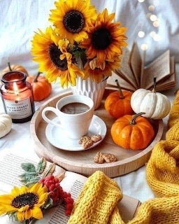 Cup of coffee on wooden tray surrounded by sunflowers, pumpkins, candle, and yellow knit blanket