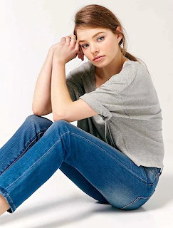 Woman in grey shirt and jeans sitting casually on white background