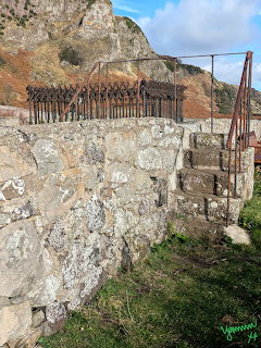 Weathered stone steps with rusted iron railing and fence on a rocky hillside in Scotland