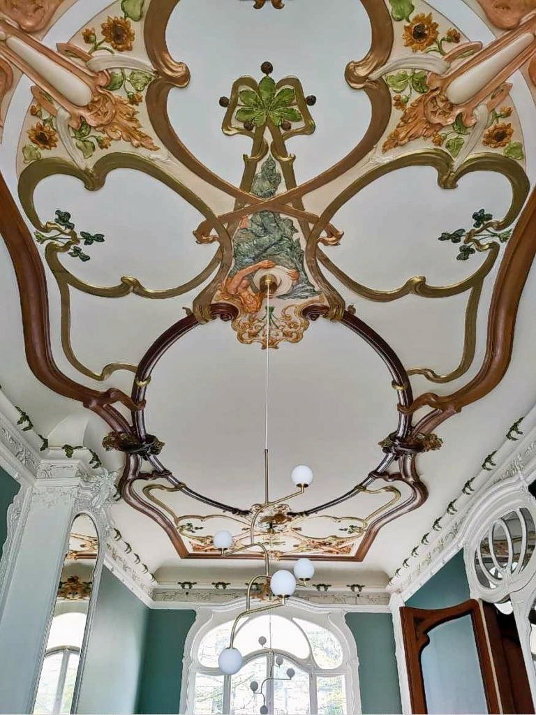 Ornate Art Nouveau ceiling with curved floral patterns and gold embellishments in turquoise room