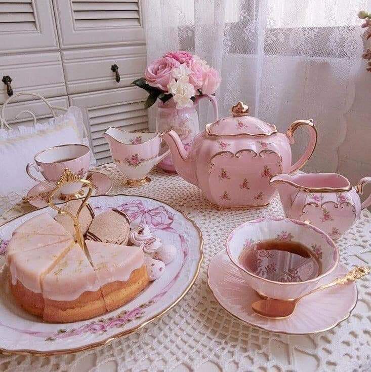 Pink teapot, teacups, and a frosted cake on a lace tablecloth in a vintage tea setting