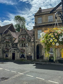 Stone building with colorful hanging flower baskets and Tudor-style architecture on a street corner under blue sky