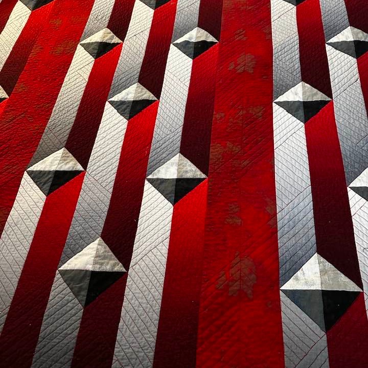 Red and white striped quilt with black geometric star pattern blocks