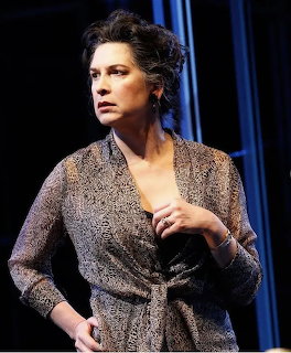 Woman with dark hair in a patterned wrap blouse performing on a dark theater stage