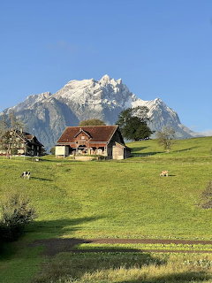 Swiss mountain chalet on green hillside with dramatic rocky peaks behind