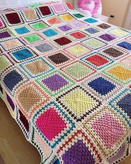 Colorful crocheted granny square blanket with white borders draped on bed