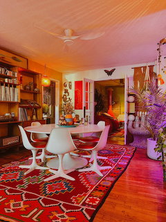 Colorful mid-century modern dining room with white tulip table, chairs, red patterned rug, and eclectic decor