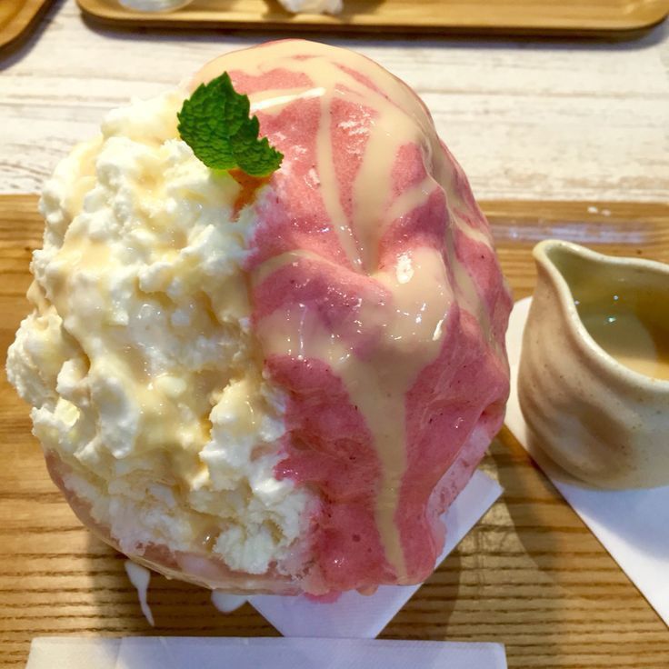 Shaved ice dessert with strawberry syrup, whipped cream, and mint garnish on wooden tray