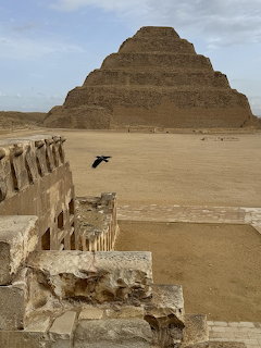 Step Pyramid of Djoser at Saqqara with desert ruins in foreground and a bird flying nearby