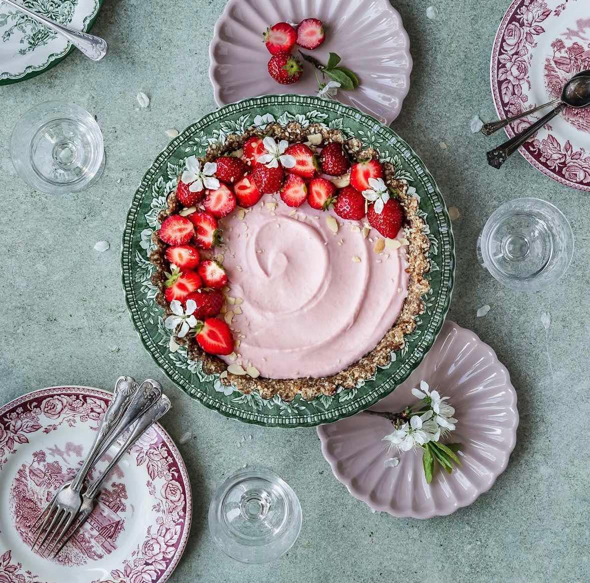 Pink frosted cake with strawberry garnish on decorative plate, overhead flat lay with pink dinnerware