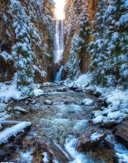 Tall waterfall in a snowy canyon with an icy stream and snow-covered trees