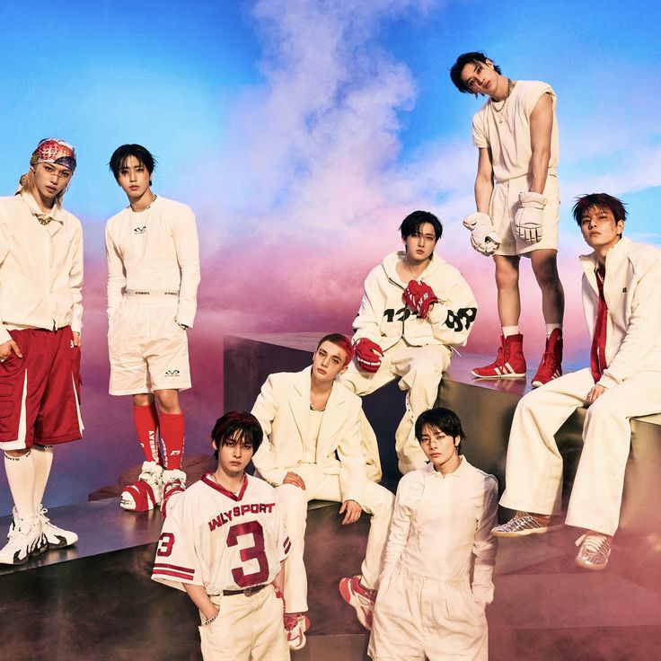 Eight young men in white outfits posed on white blocks against pink and blue sky background