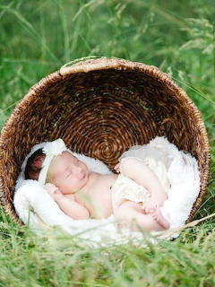 Newborn baby sleeping peacefully in a woven basket on grass, wrapped in white fabric