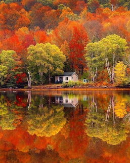 Small white house by a lake with colorful autumn trees reflected in still water