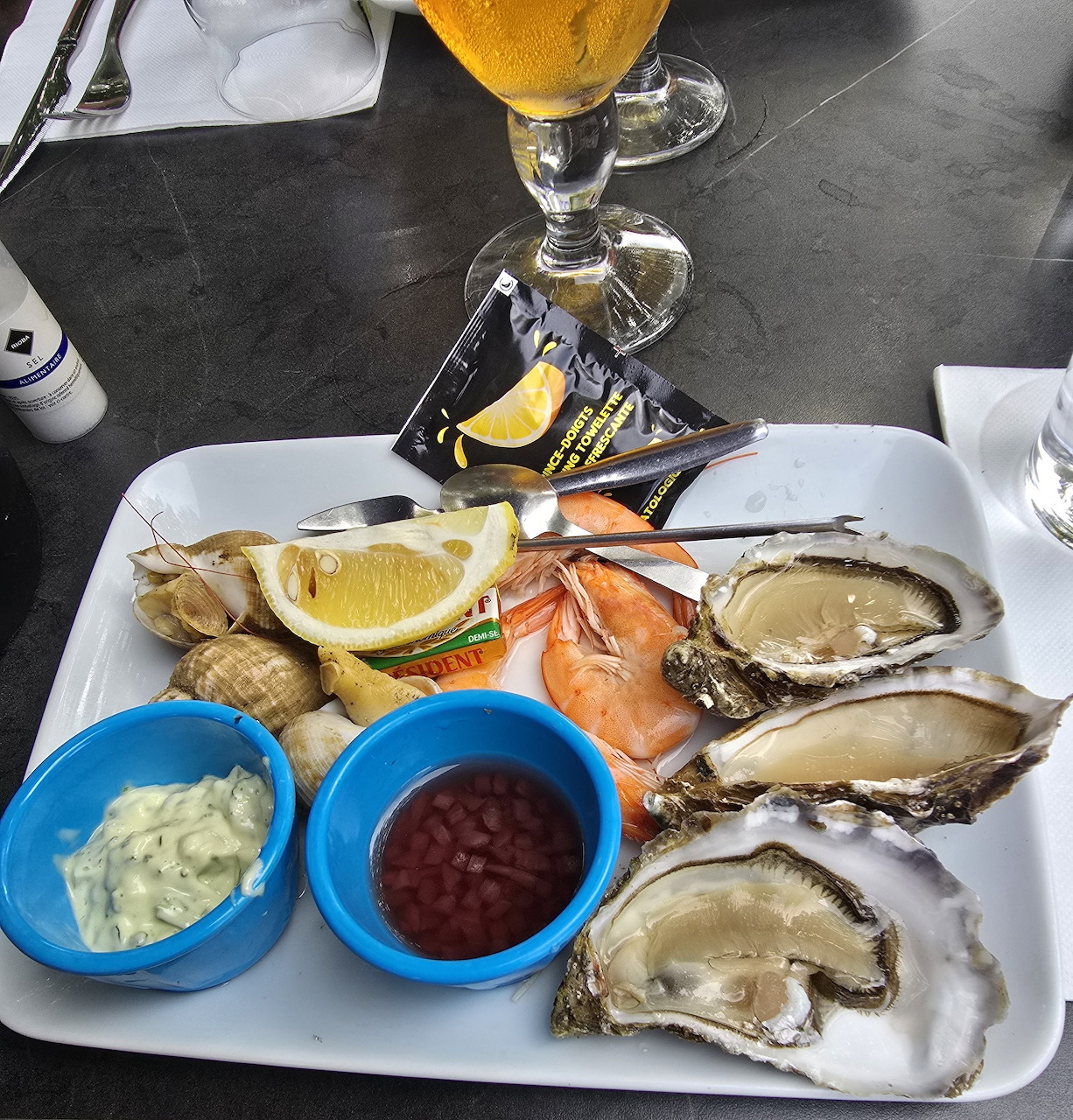 Seafood starter platter with oysters, shrimp, lemon, bread, and two sauces on a white tray