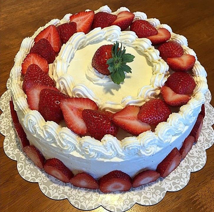 Round layered strawberry shortcake decorated with fresh strawberries and whipped cream rosettes on a white lace doily