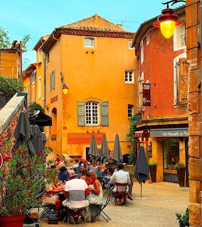 Orange and ochre buildings surrounding a sunny café terrace in Roussillon, France
