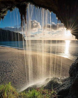 Ocean view through cave opening with waterfall and bright sunlight over calm turquoise water