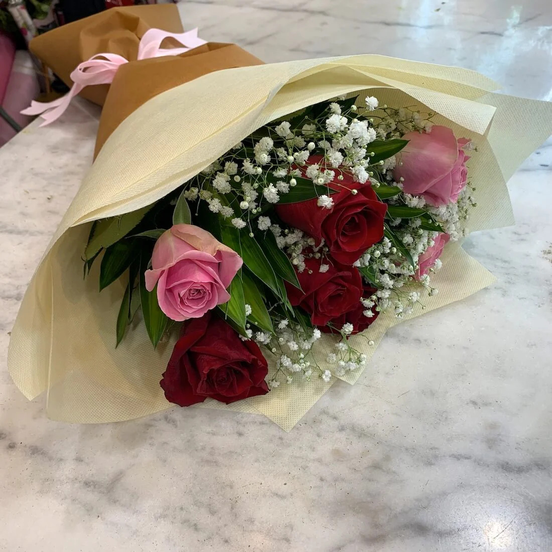 Bouquet of red and pink roses with baby's breath wrapped in beige paper on marble counter