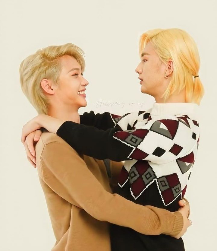 Two blonde men hugging warmly, one in tan sweater, one in checkered jacket