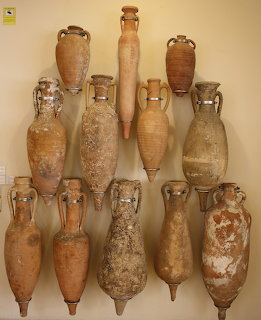Ancient clay amphorae and pottery vessels displayed on a beige wall