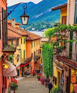 Steep cobblestone street in colorful European village with mountains and lake in background