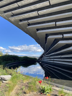 Modern angular museum building over calm waterfront with reflections and blue sky in Dundee