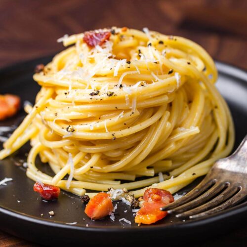 Coiled spaghetti pasta with poached egg and bacon on black plate
