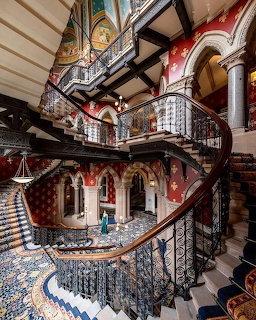Ornate Victorian spiral staircase in grand hotel interior with patterned tile floor and arched doorways