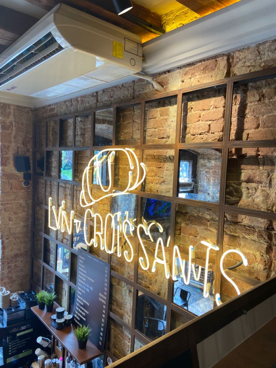 Neon sign reading Lviv Croissants on an exposed brick wall inside a cozy cafe interior