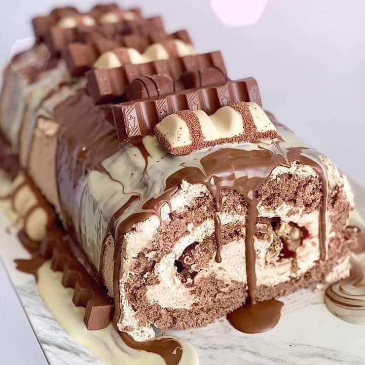 Sliced chocolate roll cake topped with candy bars and cream filling, drizzled with chocolate sauce