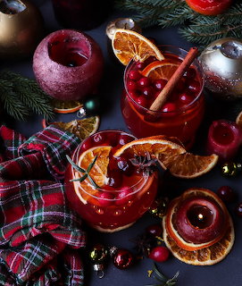 Two glasses of red cranberry sangria garnished with dried orange slices, cinnamon, and cranberries, surrounded by Christmas decor