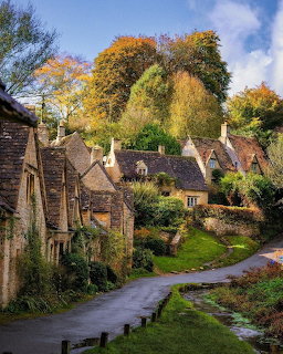 Row of old stone cottages along a narrow lane with autumn trees in an English village