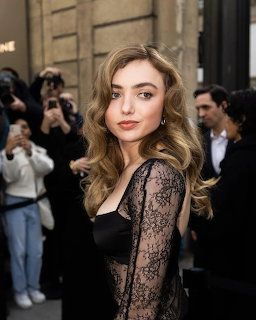 Blonde woman in black lace top posing at an outdoor event with photographers behind her