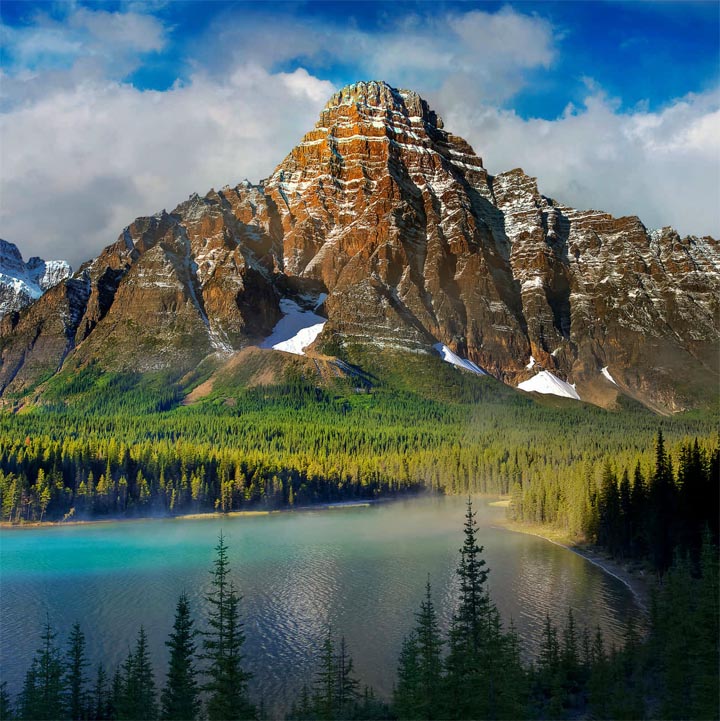 Rocky mountain above a turquoise lake with pine forest and blue sky