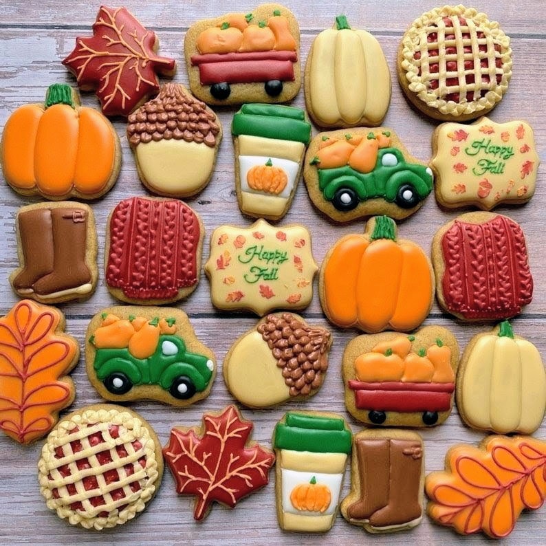 Assorted fall-themed decorated cookies with pumpkins, leaves, pies, and tractors on white wood background