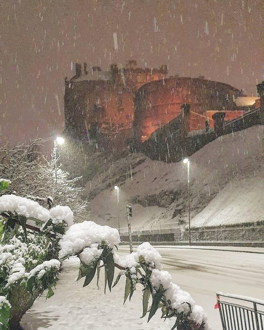 Red train in heavy snowfall at night above a snow-covered road and glowing streetlights