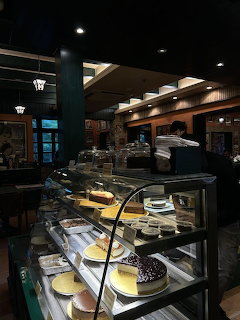 Glass display case with cakes and desserts inside a warmly lit cafe bakery