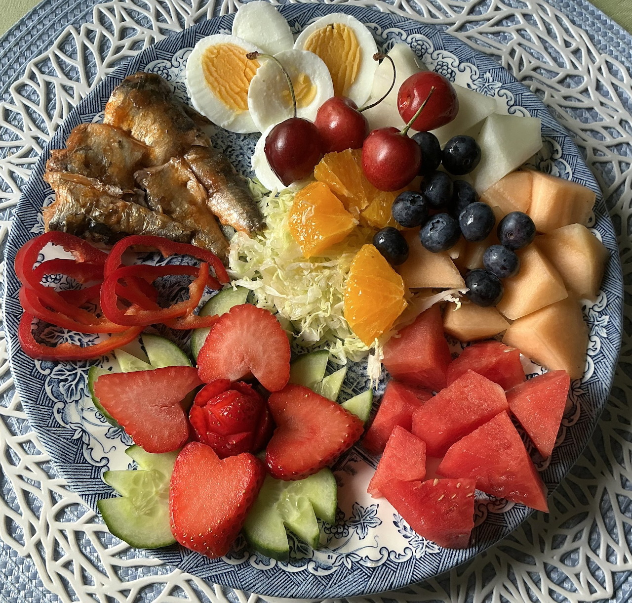 Blue patterned plate with fruit, eggs, chicken, cheese, peppers, and shredded cabbage