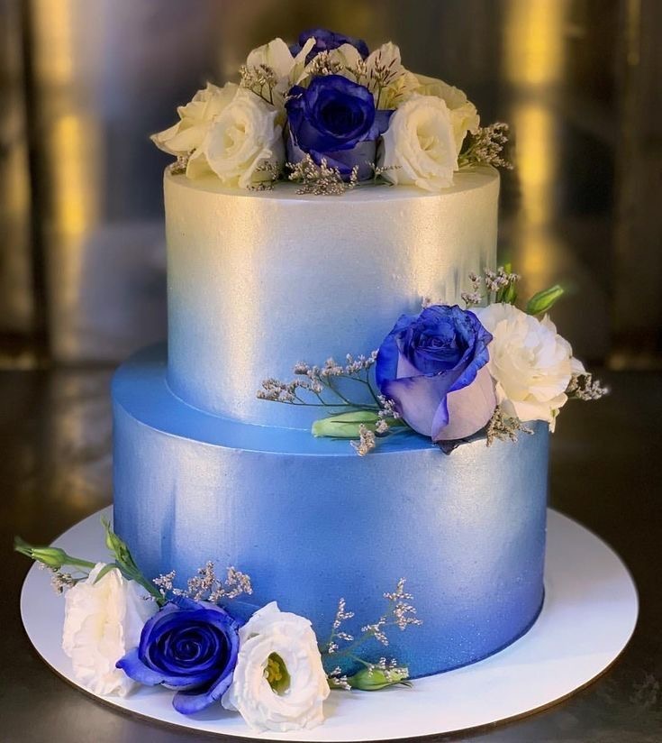 Two-tier blue ombre cake topped and decorated with blue and white roses