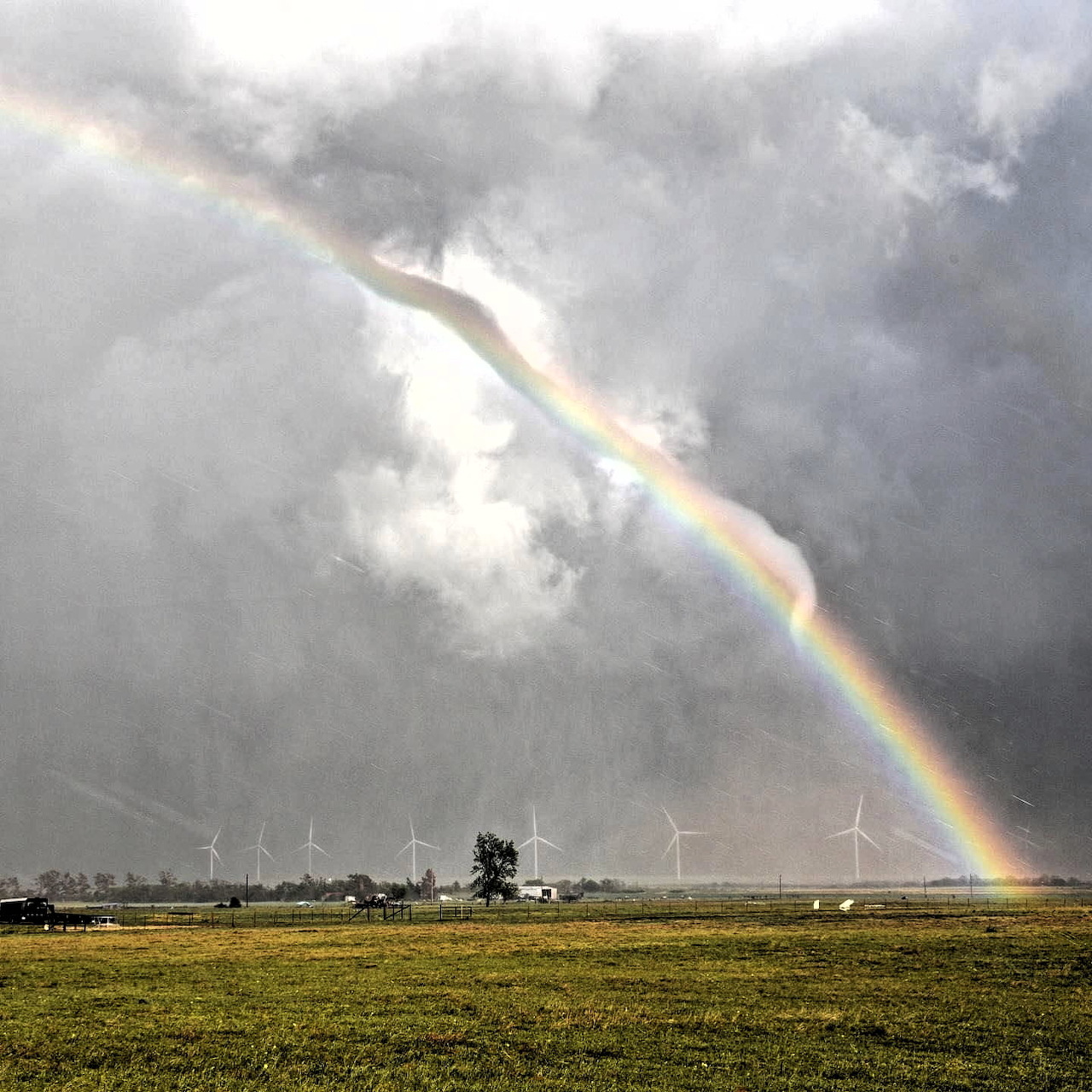 Double rainbow over stormy sky above green field with trees