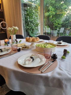 Dinner table set with plates, salad bowl, bread, candles, and pink placemats near a garden window