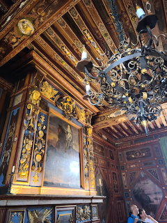 Ornate historic interior with gilded carved wooden ceiling, wrought-iron chandelier, and oil paintings on the walls