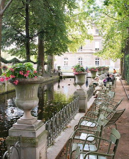 Green metal chairs lined along a pond with stone flower urns and trees at Luxembourg Garden, Paris