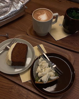 Latte with leaf art and slices of cake on plates on a wooden cafe table
