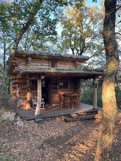 Small rustic log cabin with a wooden porch surrounded by trees in autumn