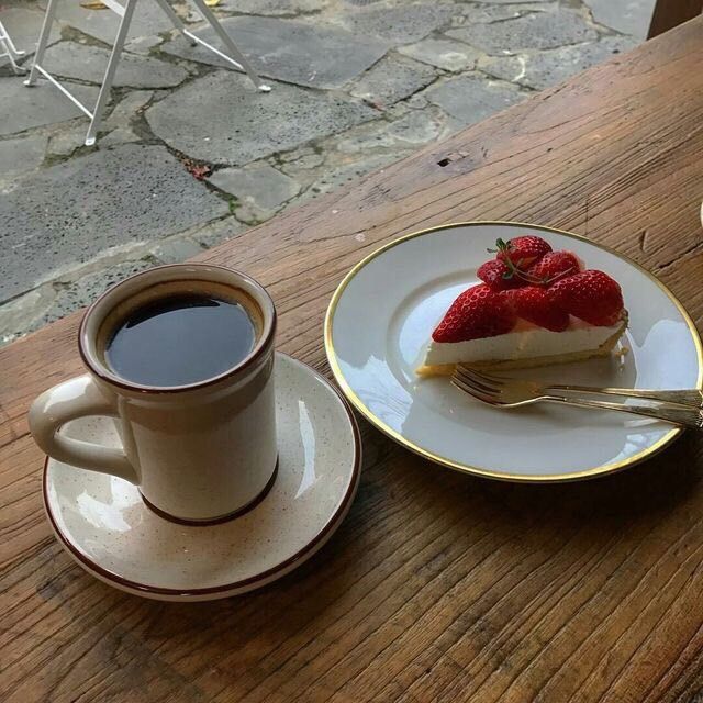 Cup of black coffee and slice of strawberry cake on wooden table
