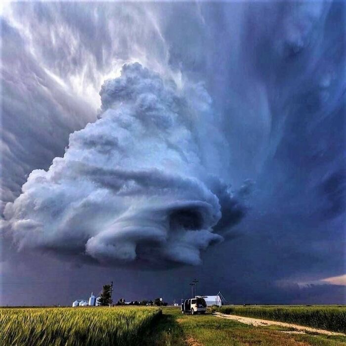 Massive supercell storm cloud formation towering over flat Kansas farmland with small buildings on horizon